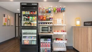 A hotel lobby with a vending machine, microwave, snack dispensers, and a Hilton Honors sign. - Spark by Hilton Asheville Blue Ridge Parkway (Asheville)