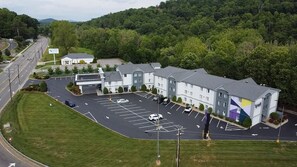 A multi-story hotel with a parking lot, surrounded by greenery and a hilly landscape. - Spark by Hilton Asheville Blue Ridge Parkway (Asheville)