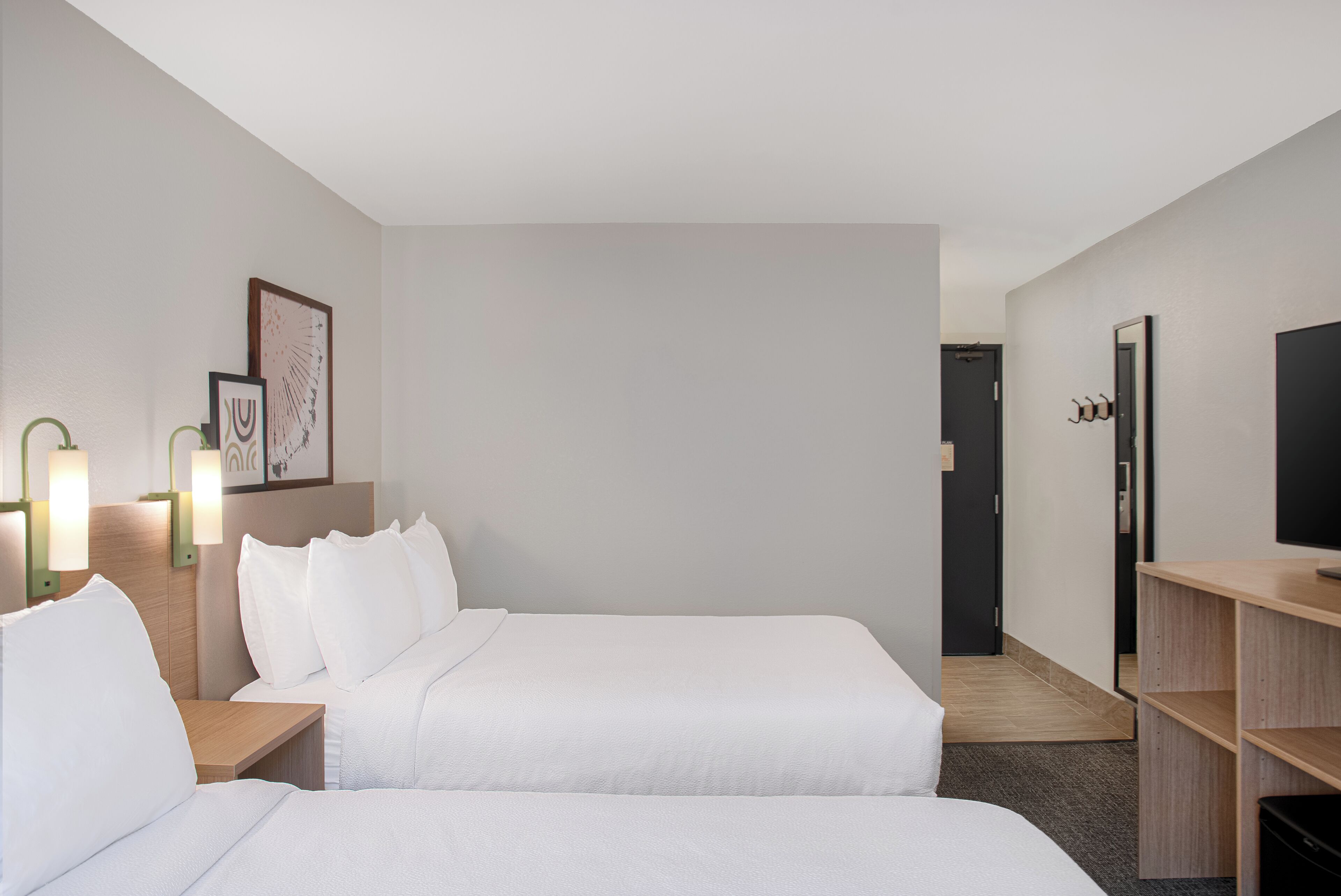 Een hotelkamer met twee bedden, een bureau, een televisie en een deur naar een gang.