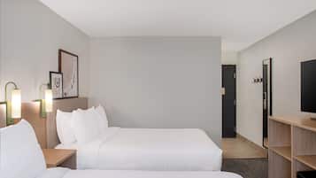 Een hotelkamer met twee bedden, een bureau, een televisie en een deur naar een gang.