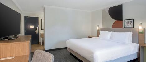 A hotel room with a bed, a desk, a chair, a television, and a wall-mounted light fixture.