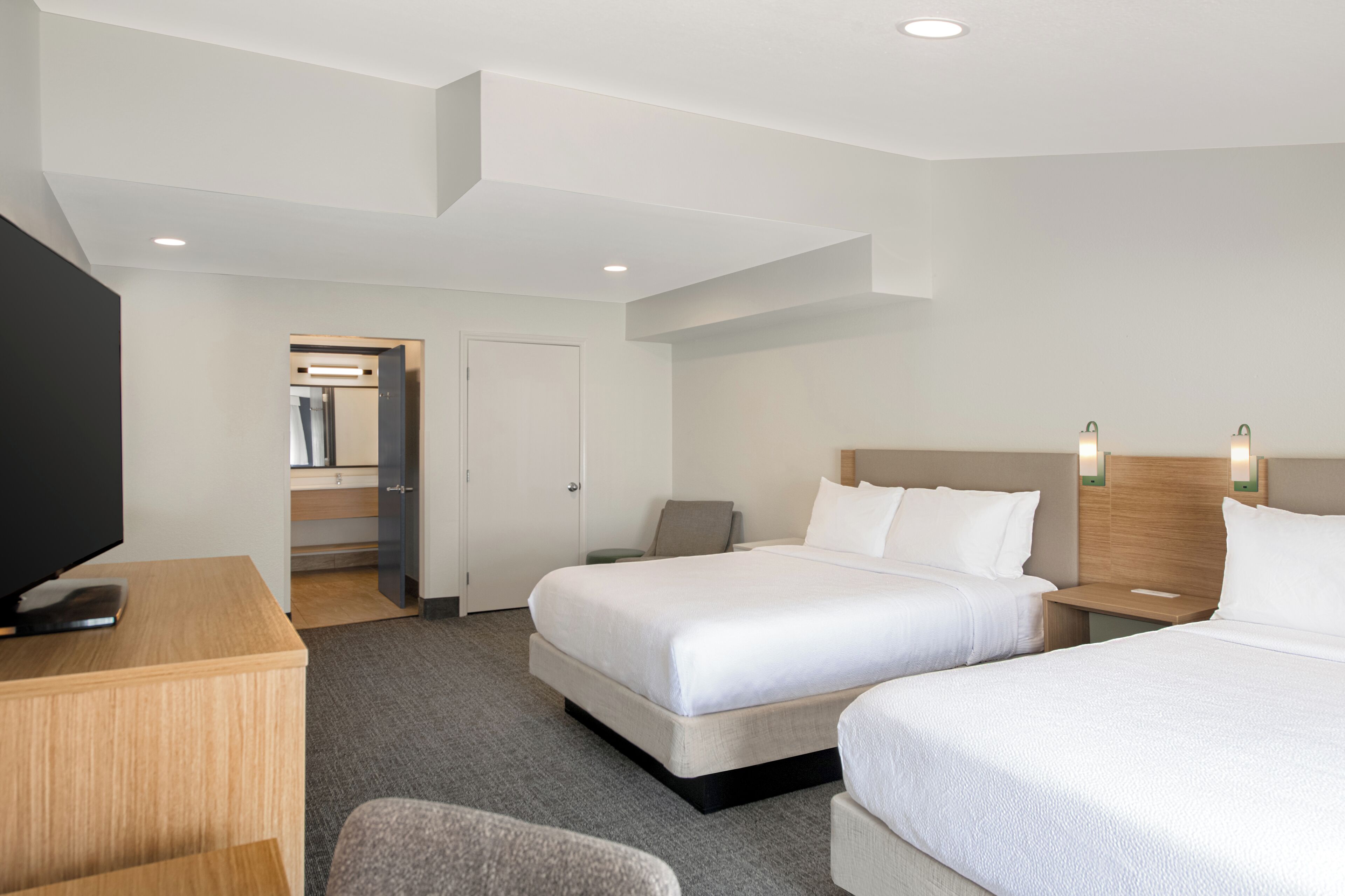 Una habitación de hotel con cama, mesitas de noche, televisor, escritorio y silla.