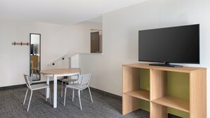A modern room with a round table, two chairs, a television on a wooden stand, and a mirror on the wall. - Spark by Hilton Asheville Blue Ridge Parkway (Asheville)