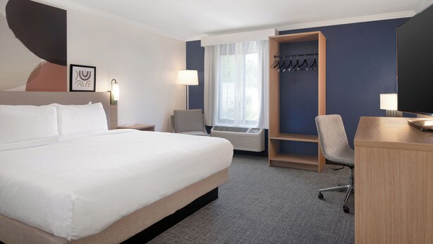 Habitación de hotel con una cama grande, un escritorio, una silla, perchero y ventana con cortinas.