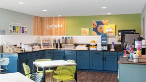 A modern café with a wooden accent wall, a menu board, and a counter with various food items and condiments. - Spark by Hilton Asheville Blue Ridge Parkway (Asheville)
