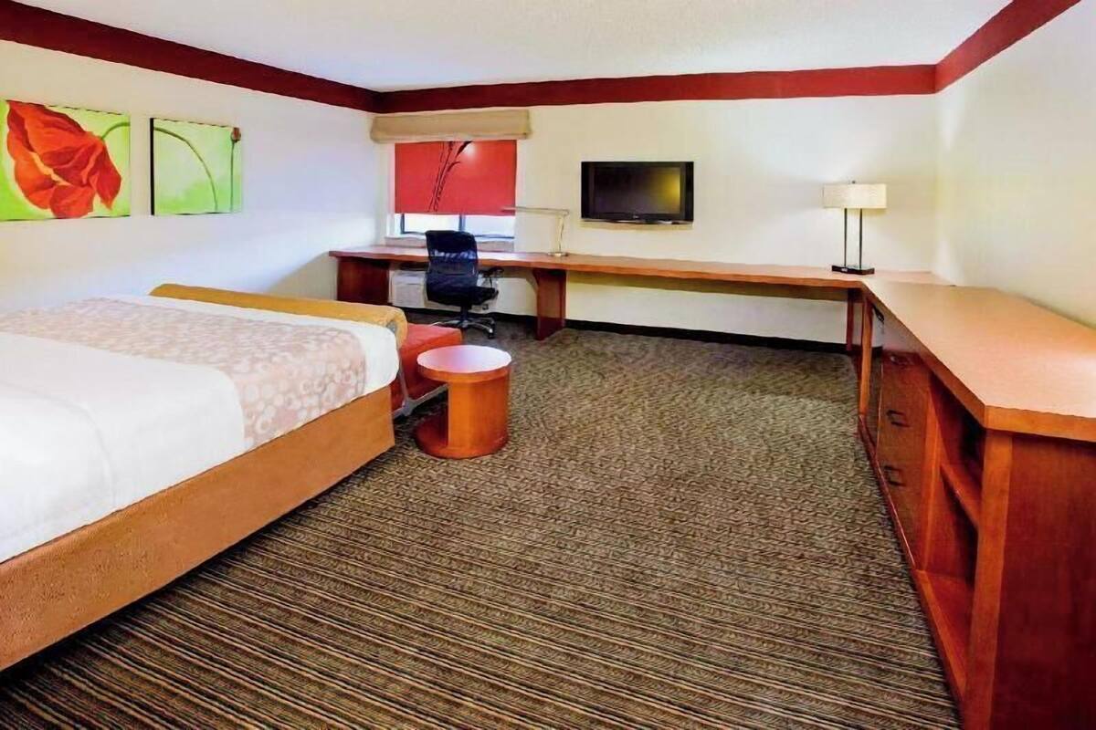 A hotel room with a bed, a desk, a chair, a television, and a lamp.