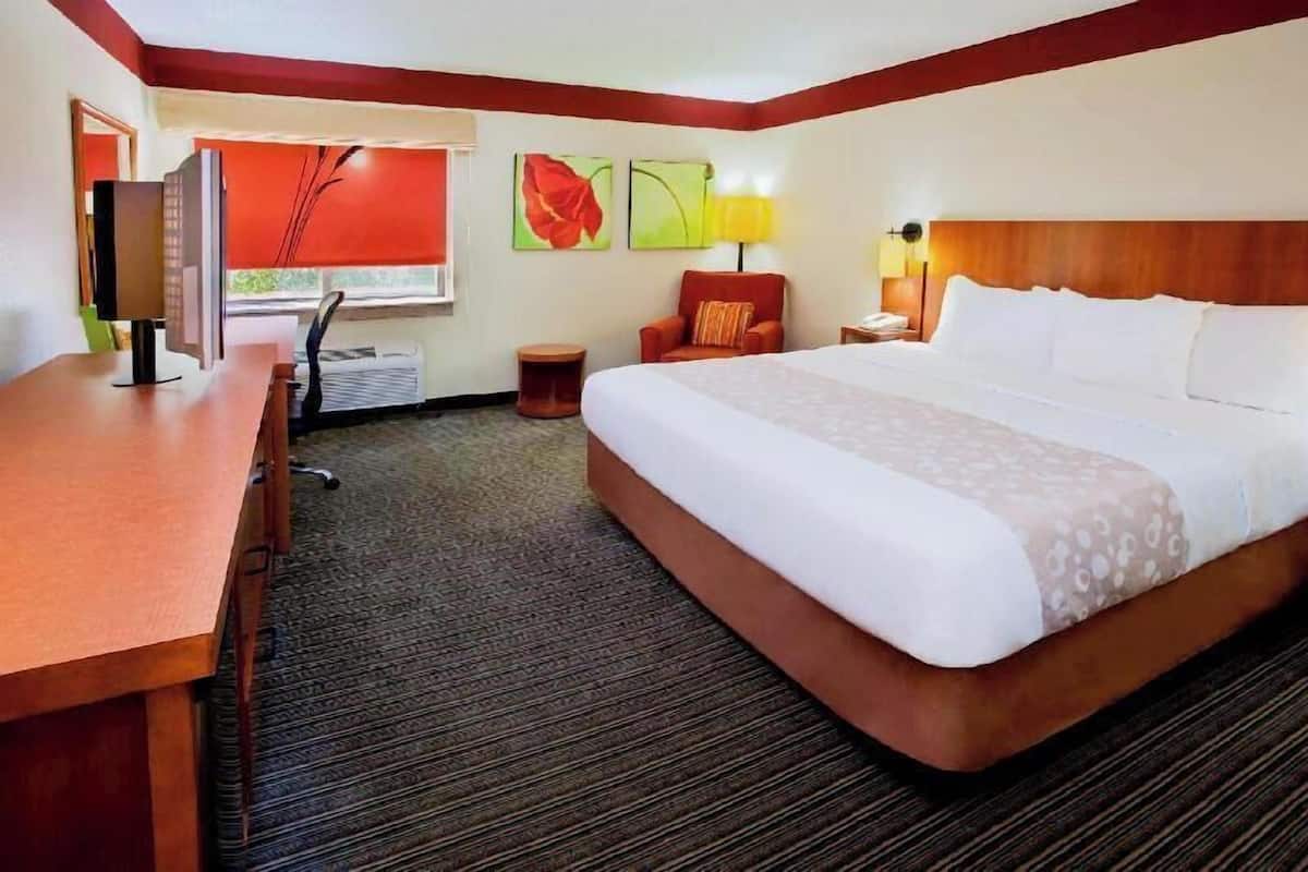 A hotel room with a bed, desk, chair, and artwork on the wall.