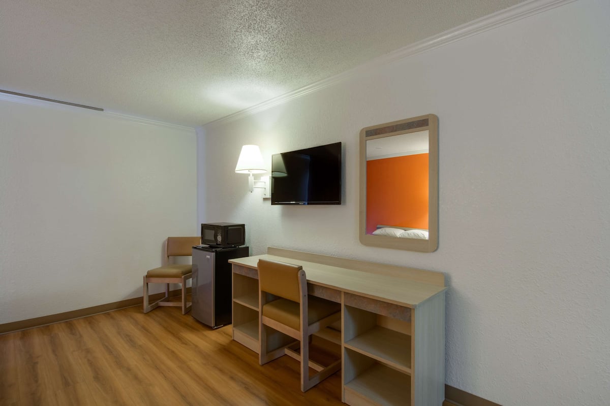 A hotel room with a desk, chair, television, and a small refrigerator.