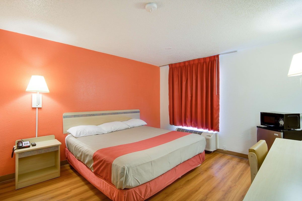 A hotel room with a bed, a desk with a lamp, a TV, and a window with curtains.