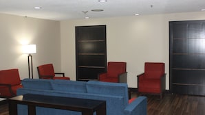 A room with a blue sofa, red chairs, a floor lamp, and dark wooden paneling on the walls. - Spark by Hilton Matteson Chicago I 57 (Matteson)