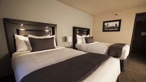 A hotel room with two beds, each with a headboard, white bedding, and a dark-colored blanket. There is a framed picture on the wall and a door to the right. - Baymont by Wyndham Glenview (Glenview)