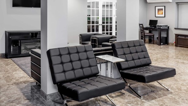 A modern lounge area with leather sofas, a fireplace, a TV, and a computer desk. - Baymont by Wyndham Glenview (Glenview)