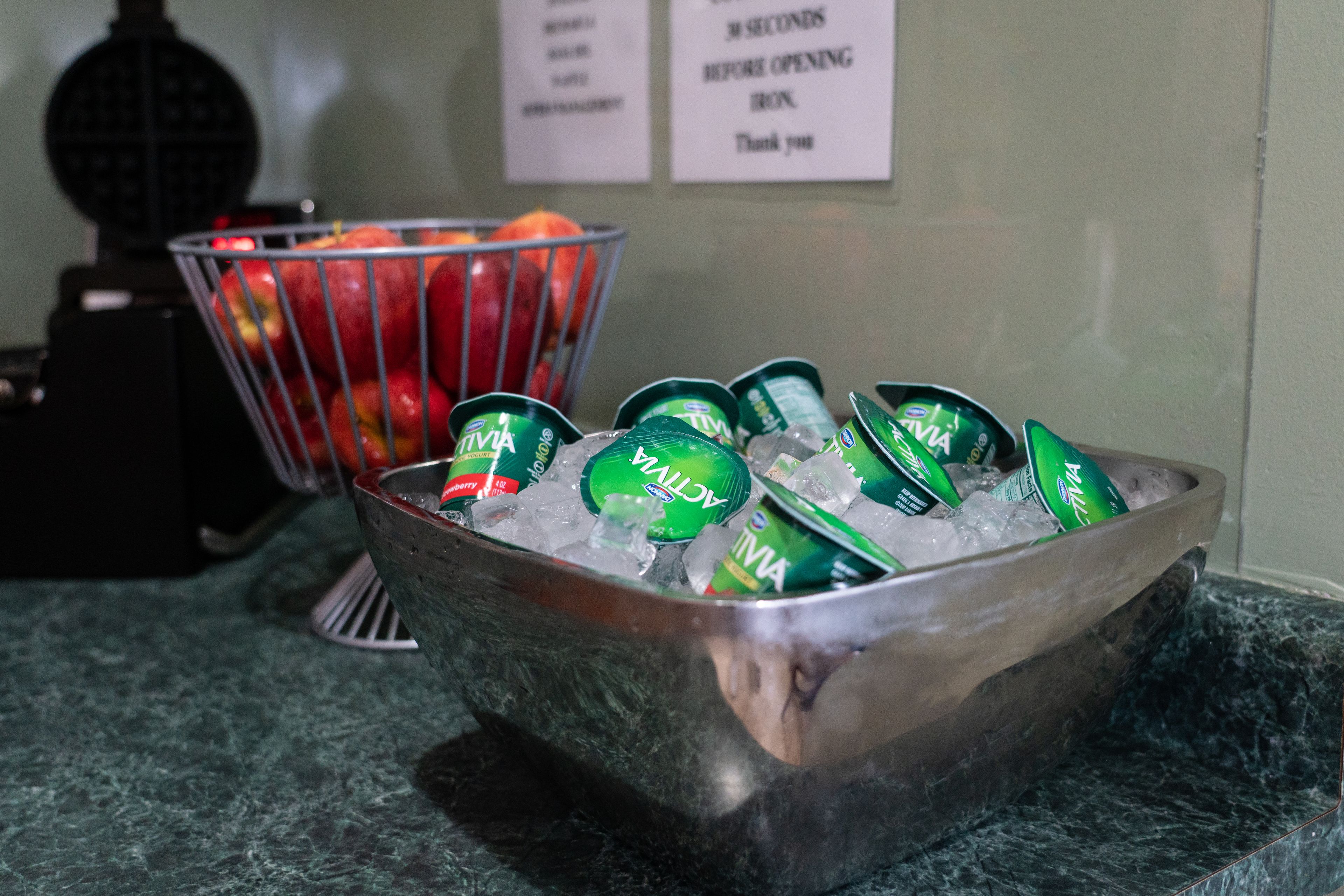 A metal bowl filled with ice and green beverage cans, placed on a marble countertop.