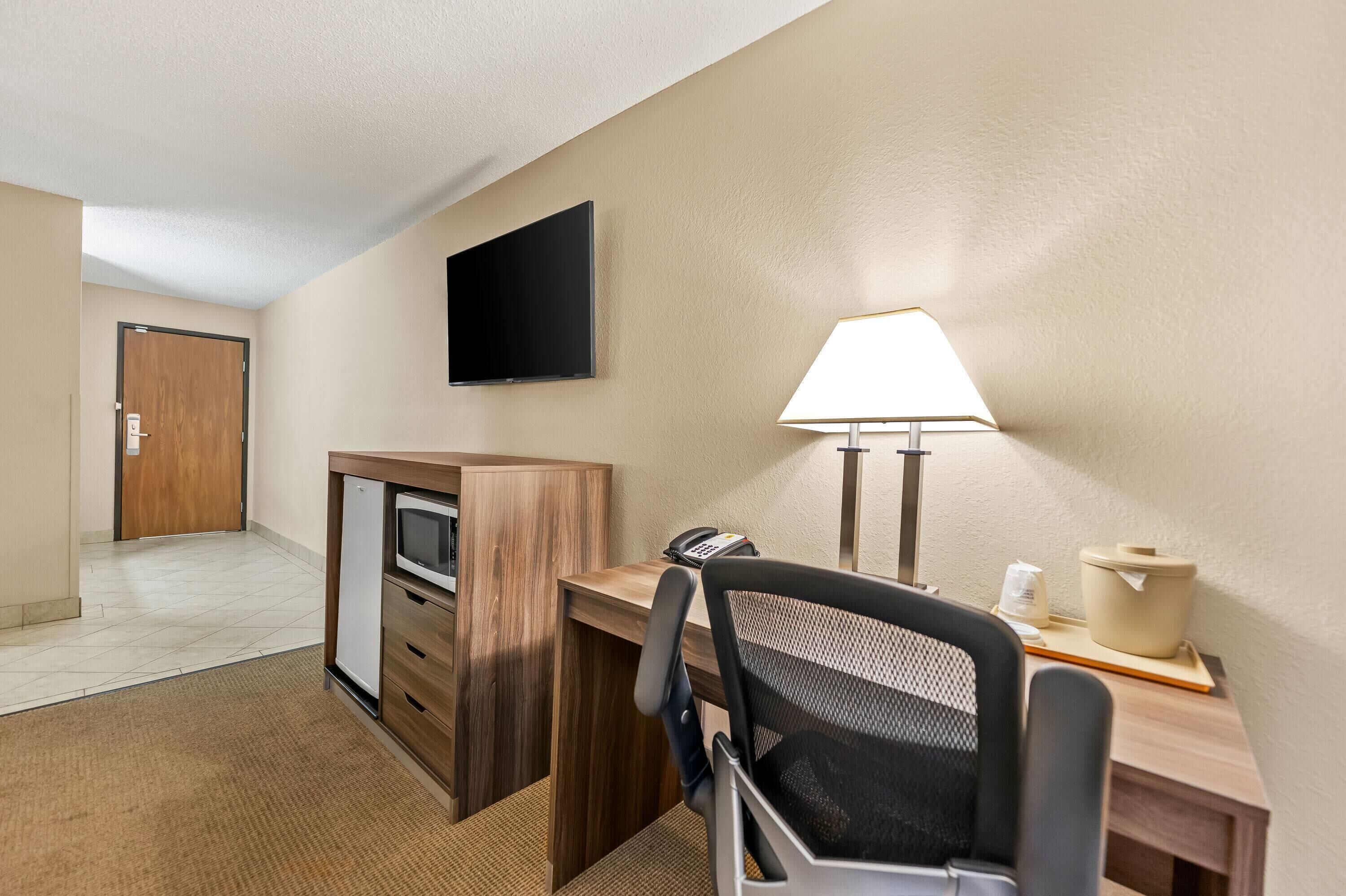 Ein Hotelzimmer mit Schreibtisch, Stuhl, Lampe, Telefon und einem an der Wand befestigten Fernseher.
