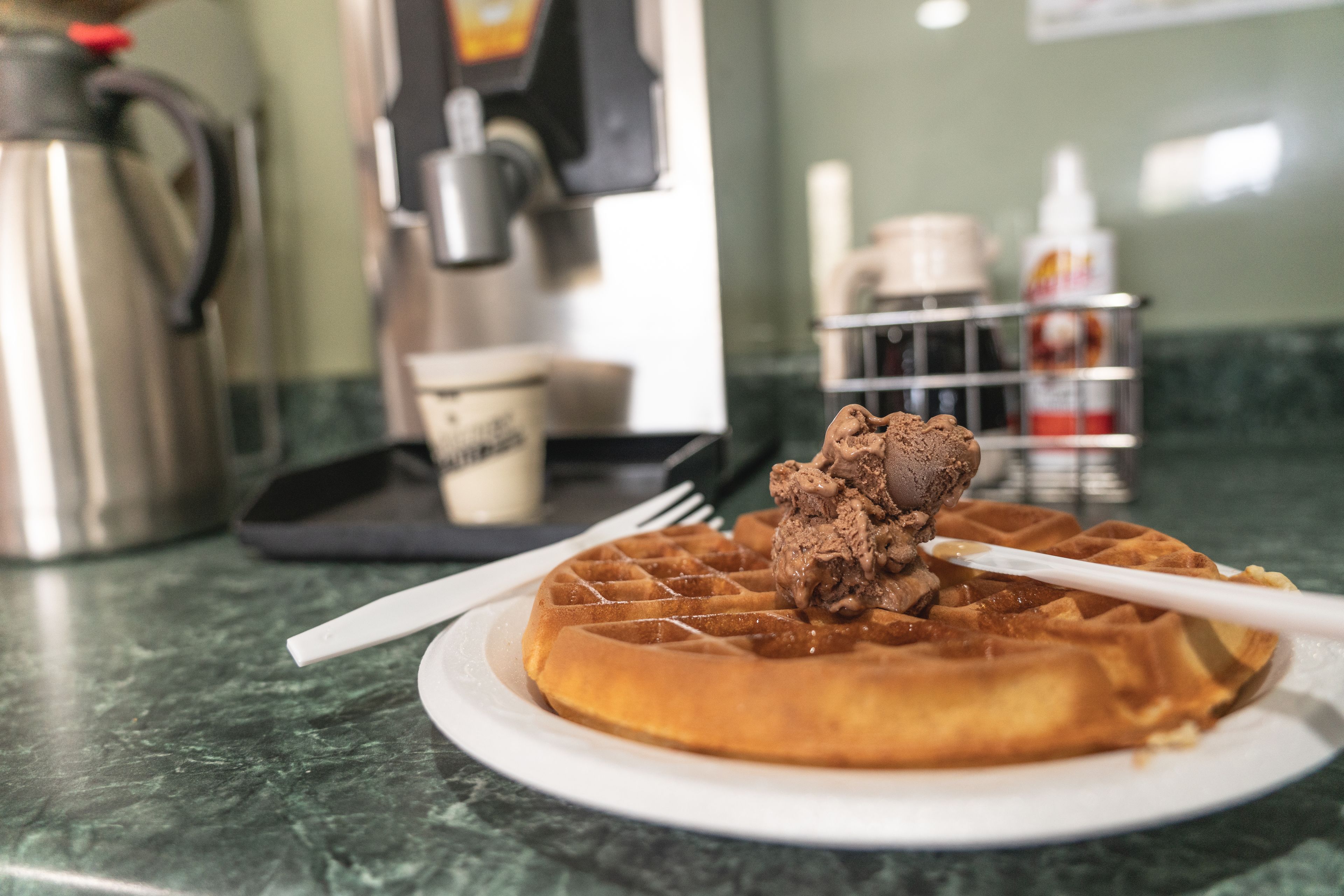 A waffle with chocolate sauce on a plate on a marble countertop.