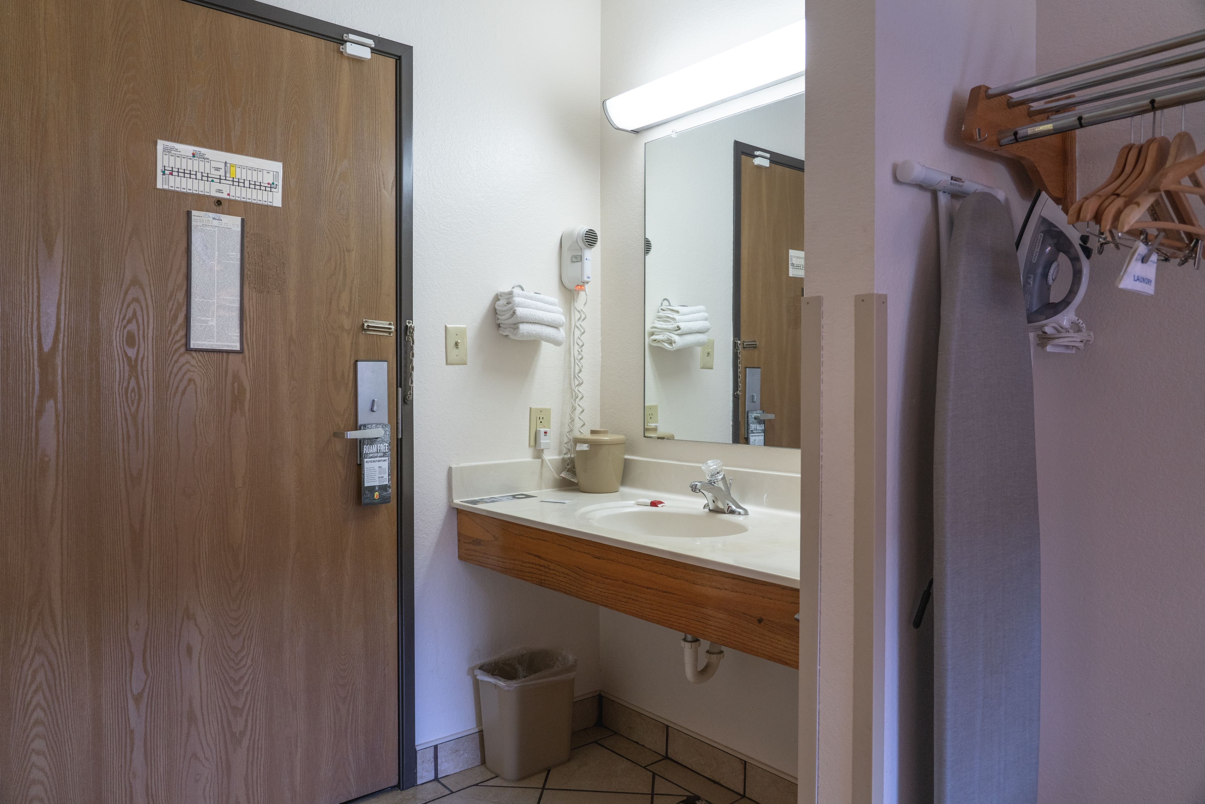 Une salle de bain avec une porte en bois, un lavabo blanc, un miroir, un sèche-cheveux et un porte-serviettes.