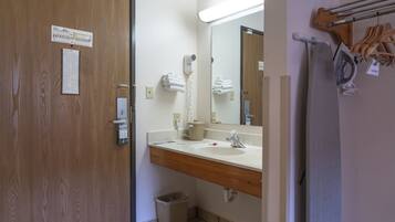Une salle de bain avec une porte en bois, un lavabo blanc, un miroir, un sèche-cheveux et un porte-serviettes.