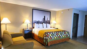 A hotel room with a bed, two bedside lamps, a chair, a nightstand, and a cityscape painting on the wall.
