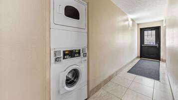 A laundry room with a front-loading washer and dryer, a door with a window, and a tiled floor.