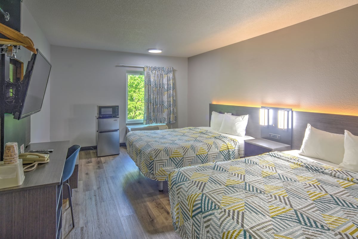 A hotel room with two beds, a desk, a chair, a television, and a window with curtains.