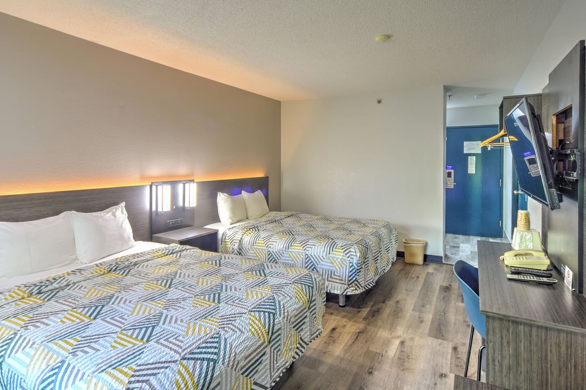 A hotel room with two beds, a desk, a chair, and a coffee machine.