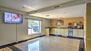 A lobby with a coffee shop, a TV screen, and a view of the outside. - Motel 6 Libertyville, IL (Libertyville)