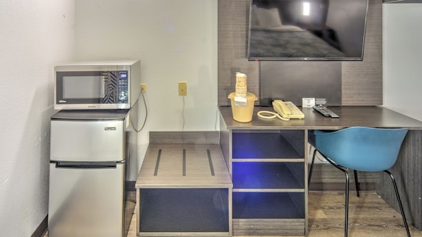 A compact kitchenette with a microwave, refrigerator, and a small dining area with a chair and a TV mounted on the wall. - Motel 6 Libertyville, IL (Libertyville)