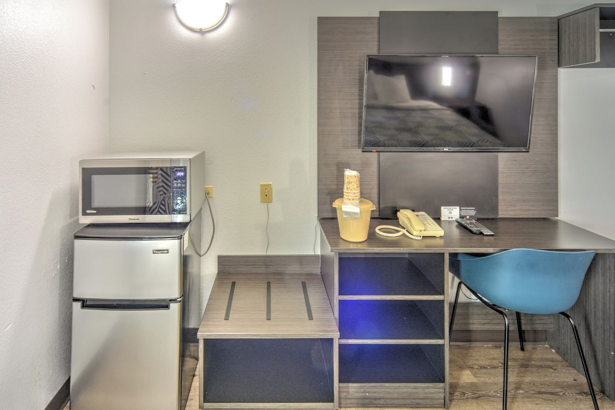 A compact kitchenette with a microwave, refrigerator, and a small dining area with a chair and a TV mounted on the wall.