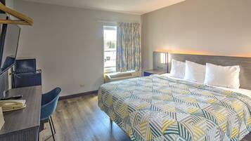 A hotel room with a bed, a desk, a chair, a window with curtains, and a nightstand.