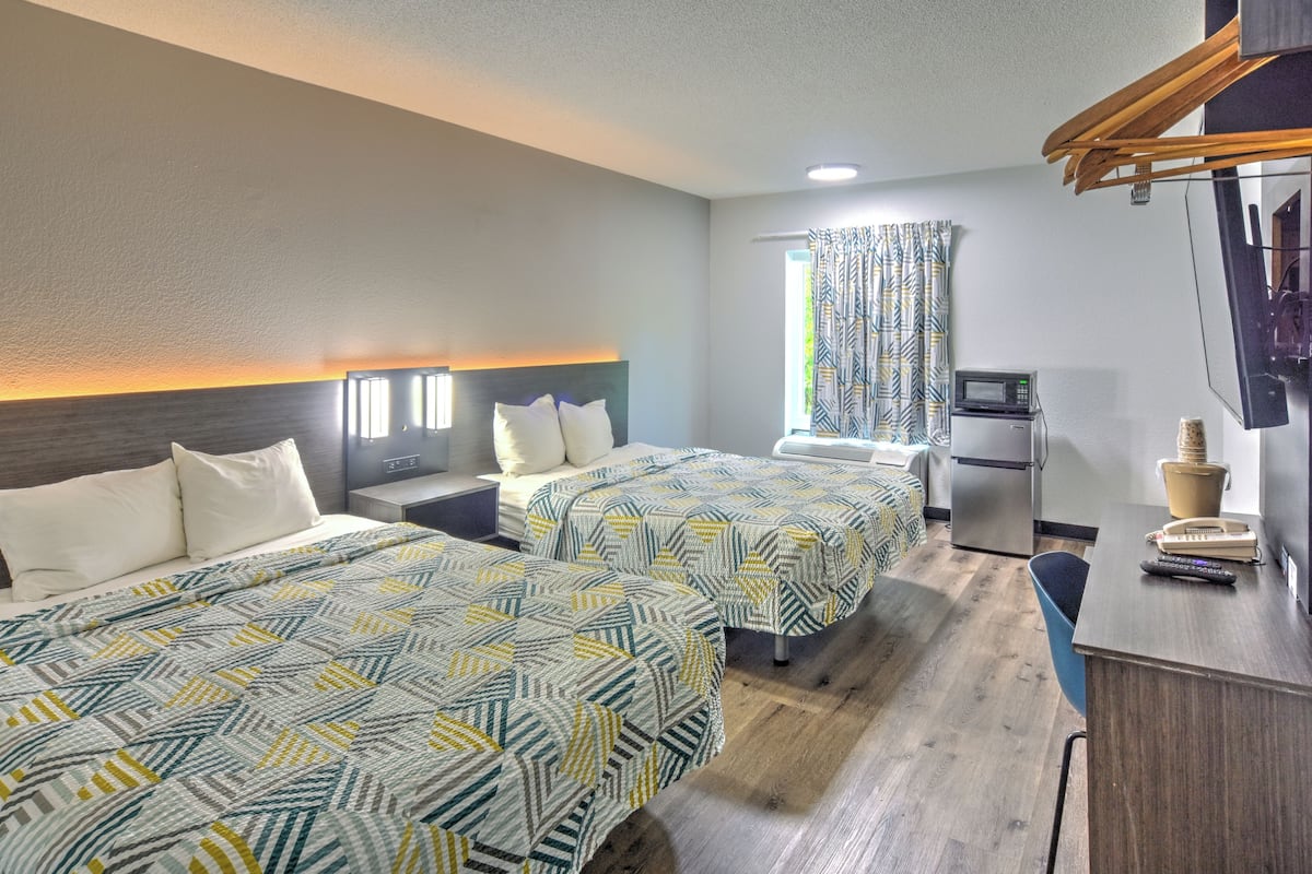 A hotel room with two beds, a desk with a telephone and remote control, a microwave, and a small refrigerator.