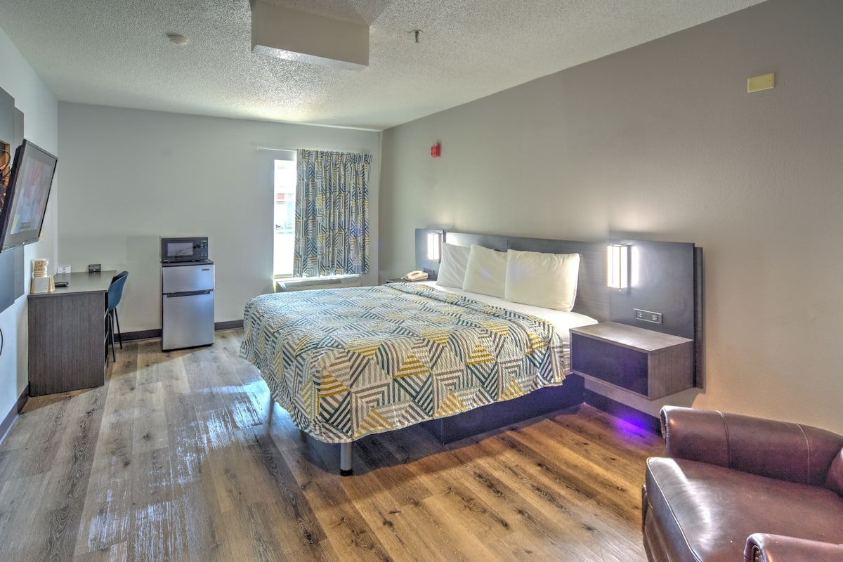 A hotel room with a bed, desk, refrigerator, and a television.