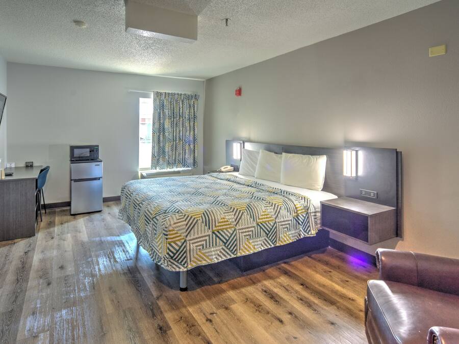 A hotel room with a bed, desk, refrigerator, and a television.