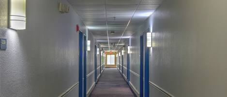 A long, narrow hotel corridor with blue doors, carpeted floors, and overhead lighting.