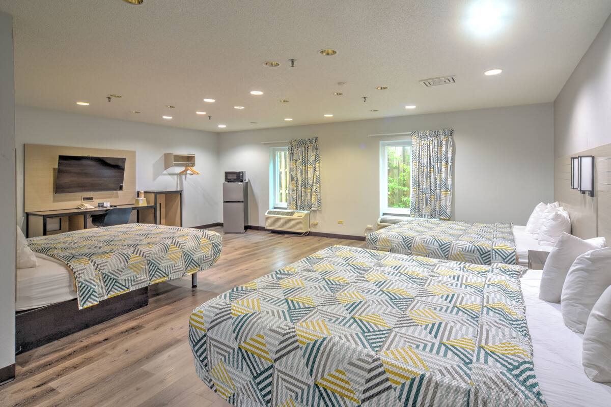 A hotel room with two beds, a desk, a TV, a refrigerator, and a window with curtains.