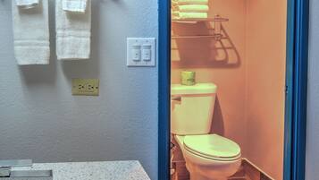 A bathroom with a white sink, two towels on a rack, a toilet, and a door leading to another room.