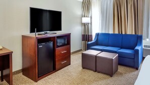 A hotel room with a flat-screen TV, a minibar, a blue sofa, and a small table. - Comfort Inn Hoffman Estates - Schaumburg (Hoffman Estates)