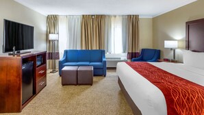 A hotel room with a bed, a blue sofa, a desk with a TV, and a lamp. - Comfort Inn Hoffman Estates - Schaumburg (Hoffman Estates)