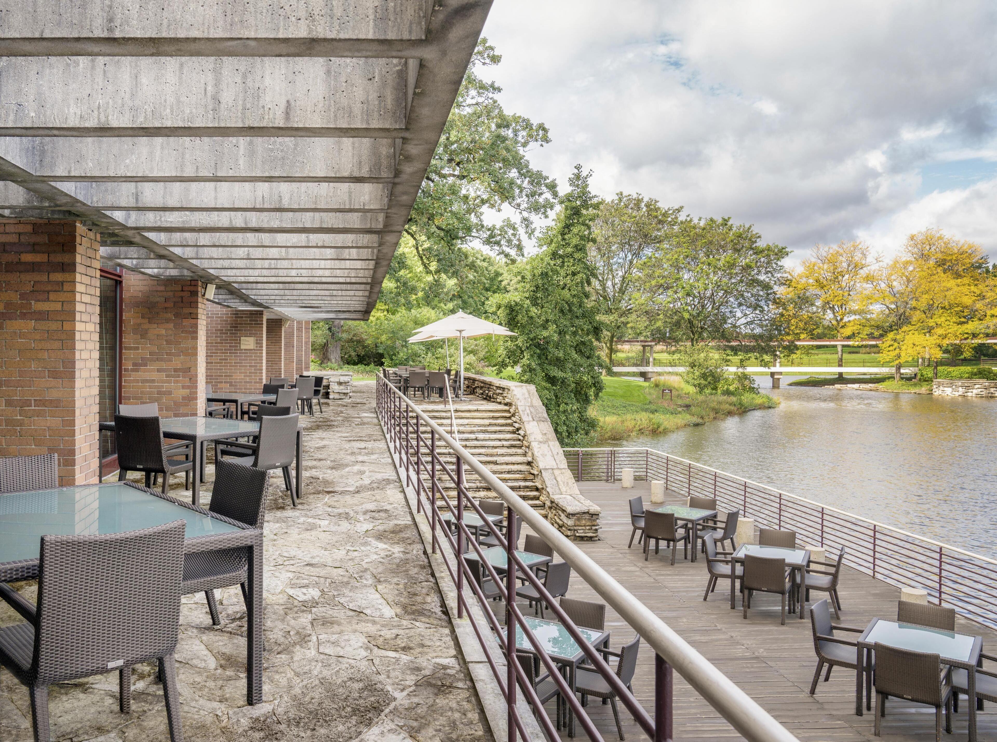 Un patio esterno con tavoli e sedie, un vialetto in pietra e vista su un fiume e un parco.