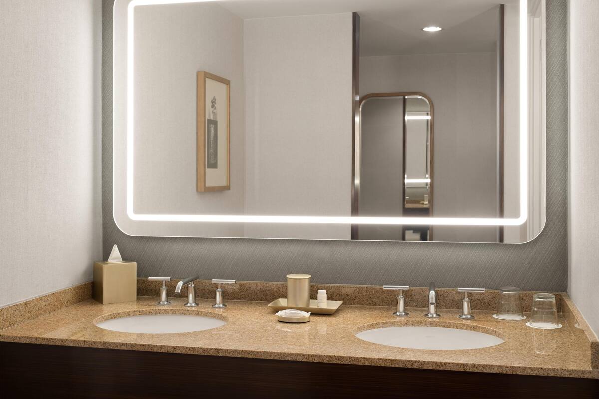 A bathroom with two sinks, a large mirror with LED lighting, and a framed picture on the wall.