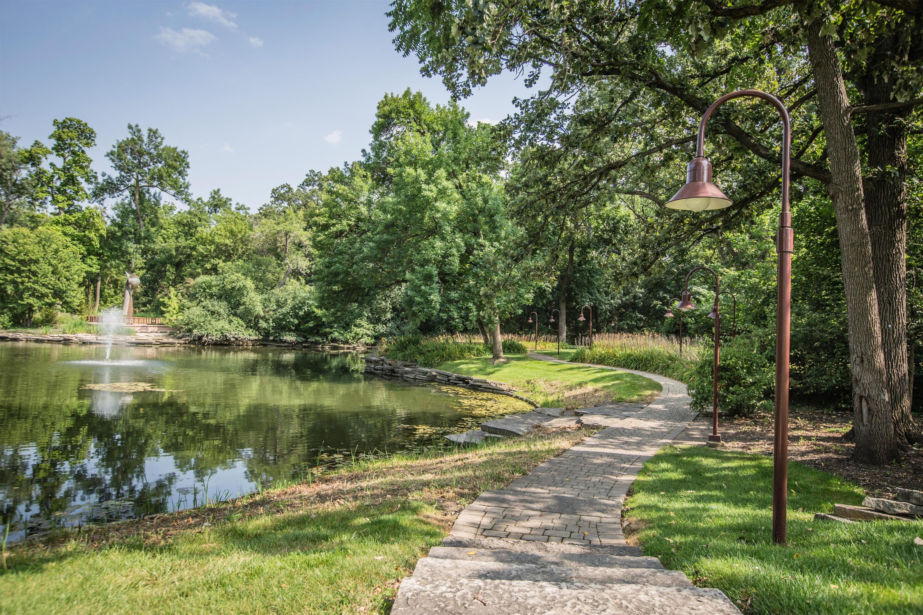 A park with a pond, a pathway, and a lamp post.