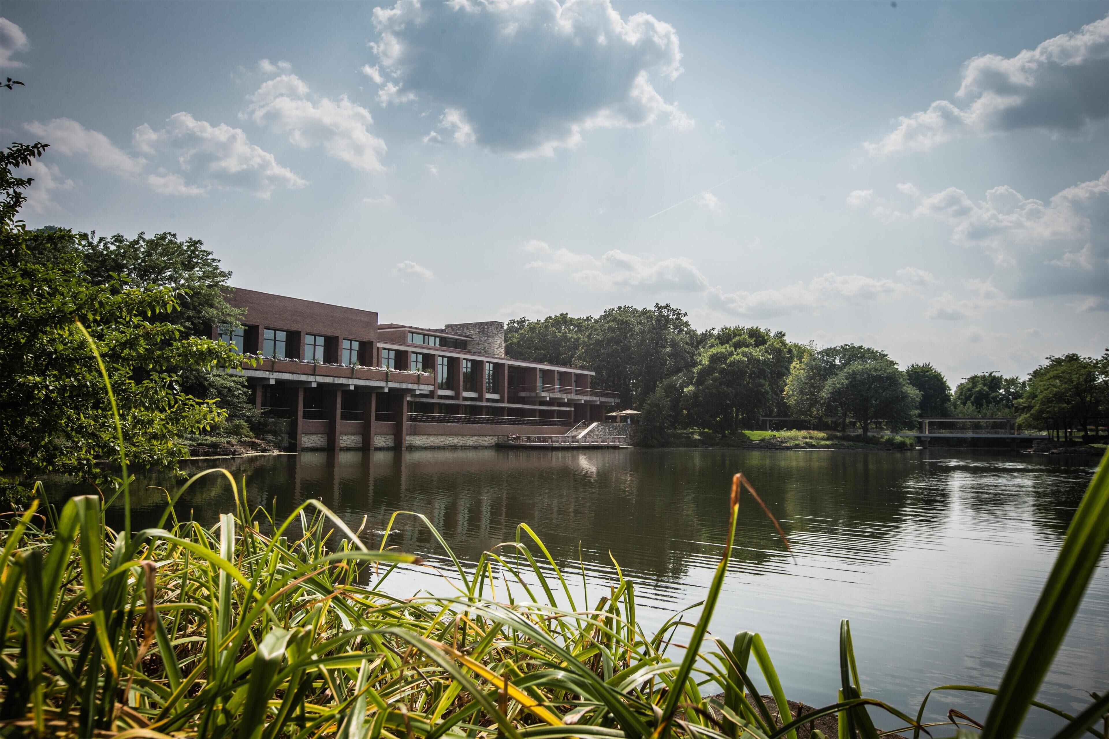 A building with a modern architectural style, a body of water in the foreground, and a bridge in the background.