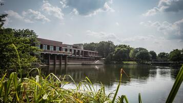 A building with a modern architectural style, a body of water in the foreground, and a bridge in the background.