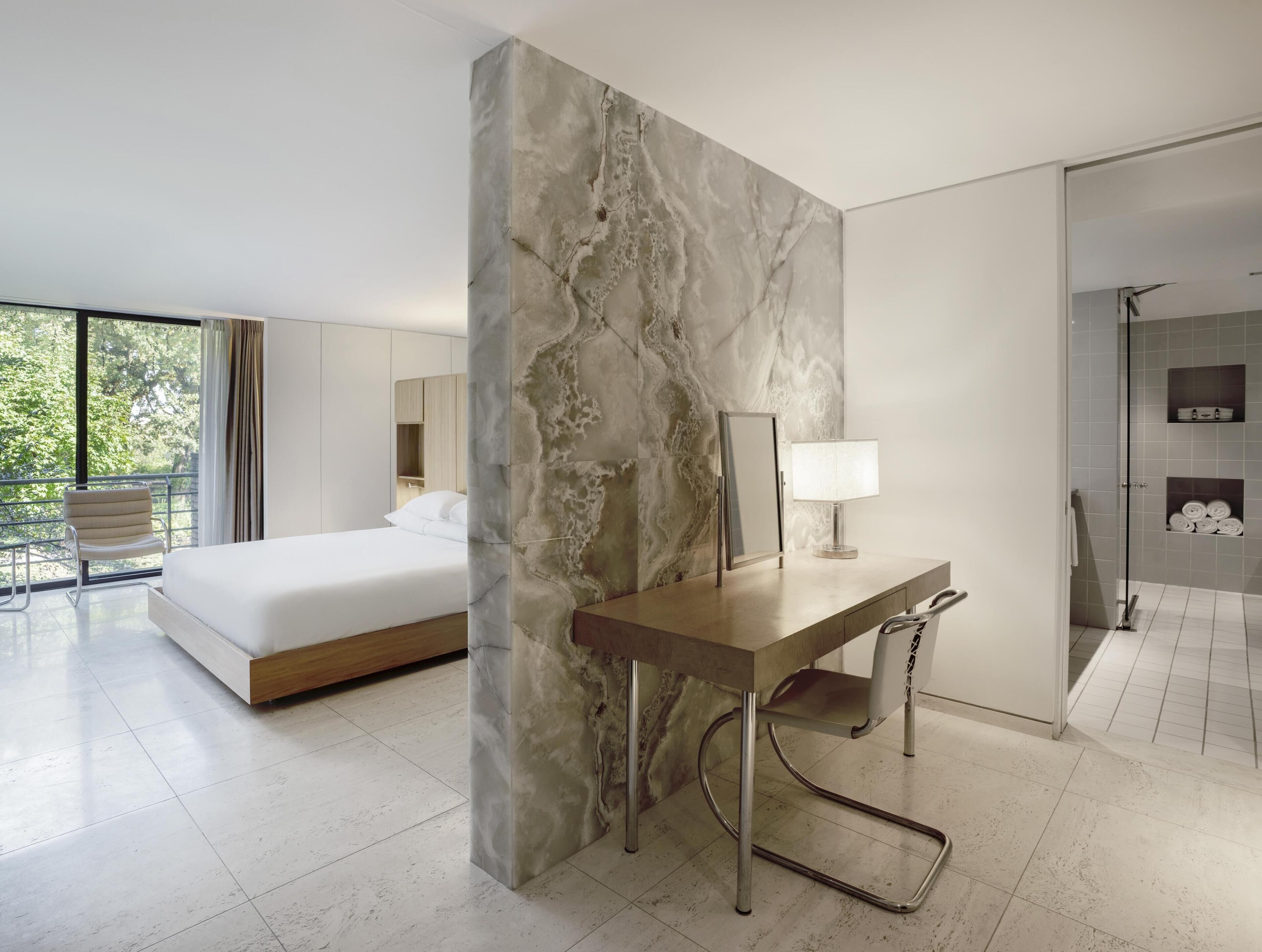 A modern hotel room with a bed, desk, and shower area.