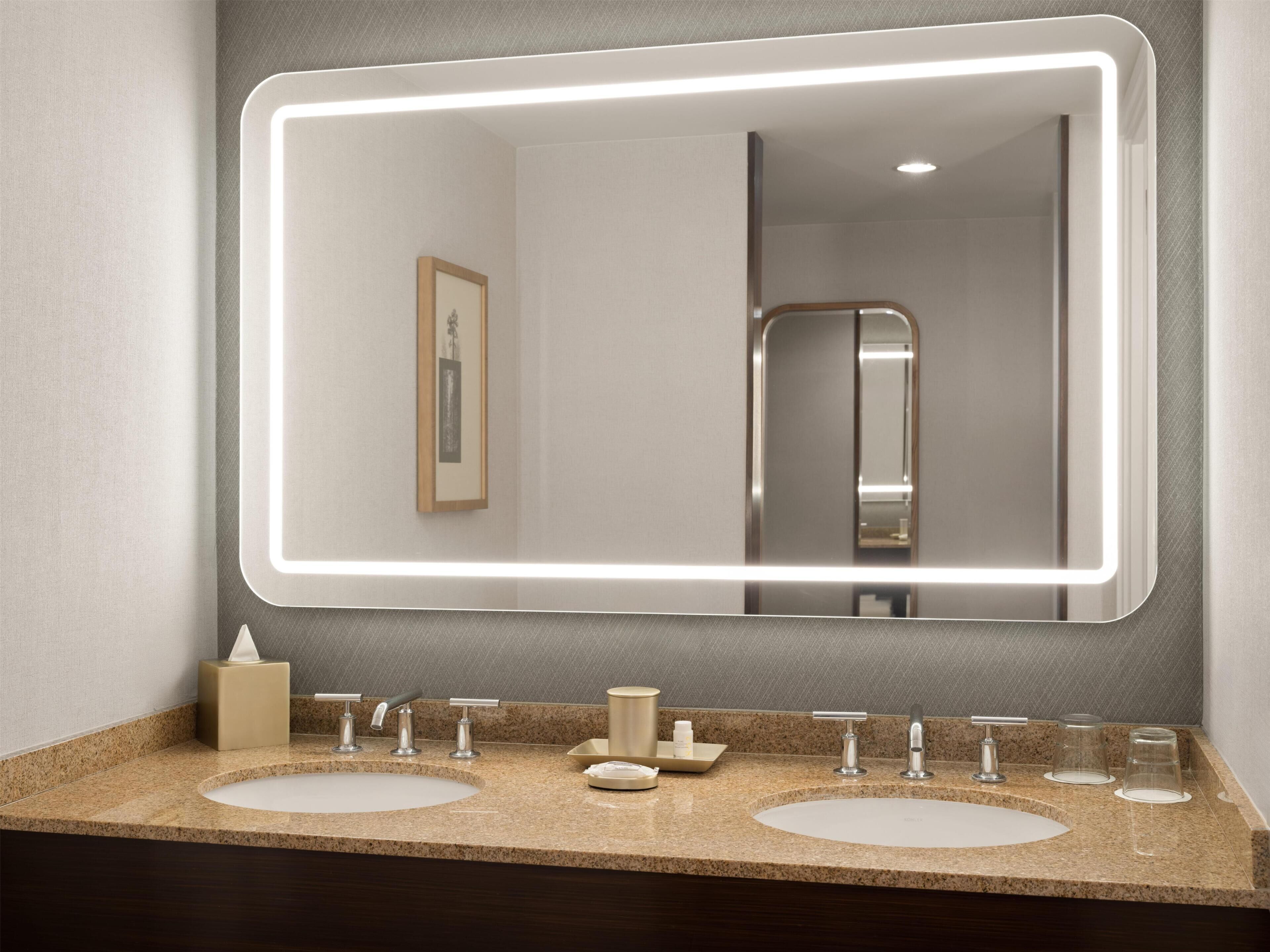 A bathroom with two sinks, a large mirror with LED lighting, and a framed picture on the wall.