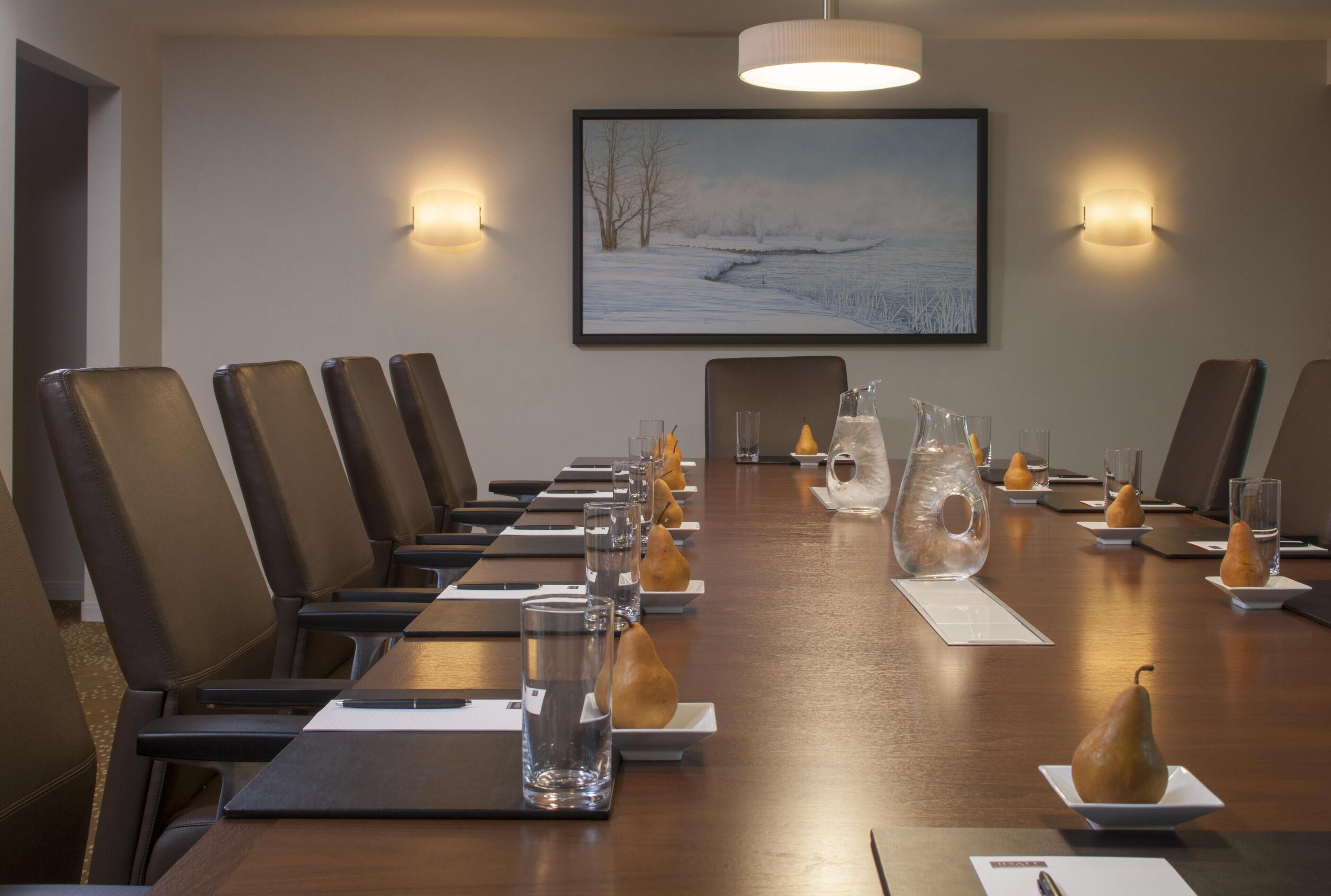 Een vergaderruimte met een lange tafel, stoelen, waterglazen en decoratieve peren.