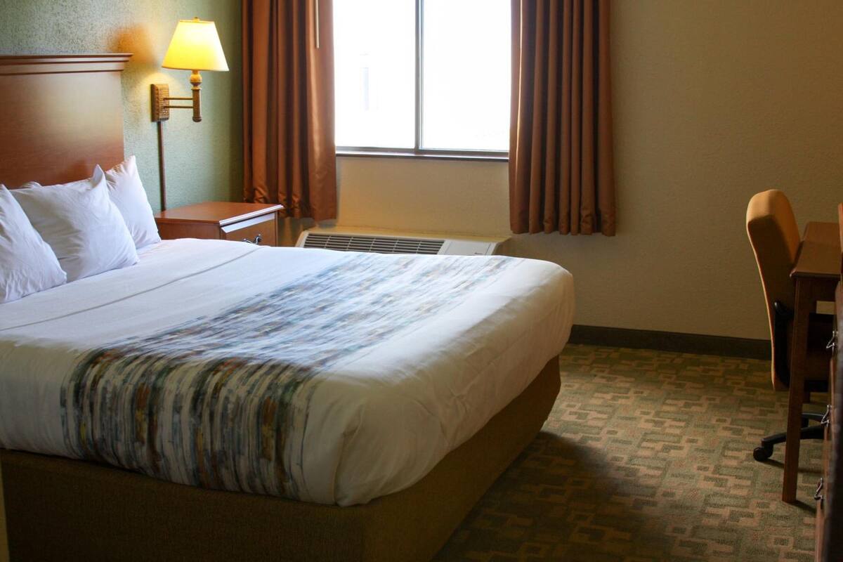 A hotel room with a large bed, a desk, a chair, a lamp, and a window with curtains.