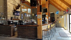 A bar area with a stone wall, wooden ceiling, and a mounted deer head.