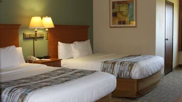 A hotel room with two beds, a nightstand with a lamp, a painting on the wall, and a door.