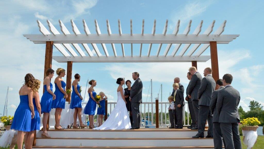 A wedding ceremony under a white pergola with a clear sky.