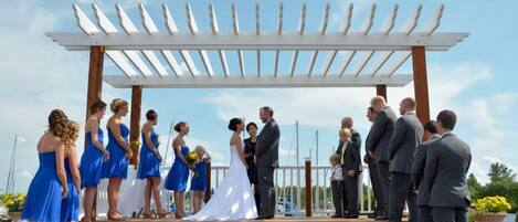 A wedding ceremony under a white pergola with a clear sky.